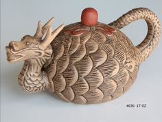 a ceramic teapot with a dragon design on the front and sides, sitting on a white surface