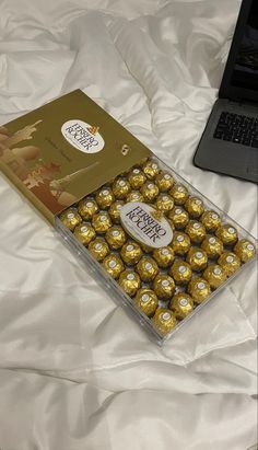 a laptop computer sitting on top of a bed next to a box of chocolates