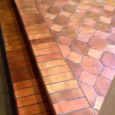 an orange cat sitting on the ground next to a wooden bench and brick flooring