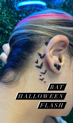 the back of a woman's ear with bats on it and behind her ear is a neon sign that says bat halloween flash