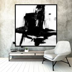 an abstract black and white painting hangs on the wall next to a modern style chair