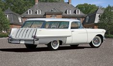 an old white station wagon parked in front of a large house