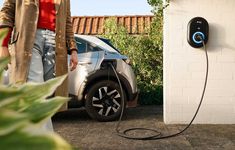 an electric car plugged in to a wall next to a woman standing near it