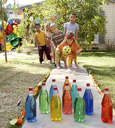 children are playing with water bottles on a table in front of a house that is decorated with balloons and streamers