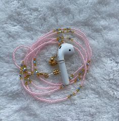 a white earphone on a pink beaded lanyard with gold bells and beads