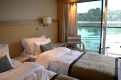 two beds in a hotel room next to a large window with a view of the water