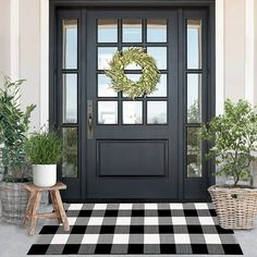 a black door with a wreath on it and two potted trees in front of it