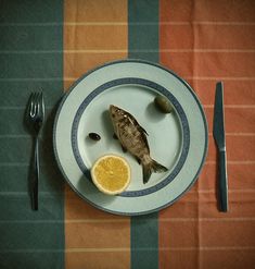 a fish on a plate next to a fork and knife with an orange slice in it