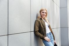 a woman leaning against a wall with her hand on her hip and looking at the camera