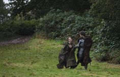 two people dressed in medieval clothing are walking through the grass