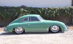 an old green car parked in front of a hedge