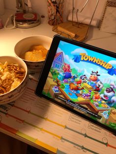 a tablet sitting on top of a table next to bowls of food and a bowl of chips