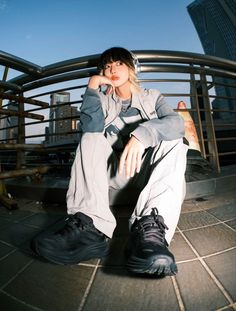 a young woman sitting on the ground with her hand under her chin and looking up