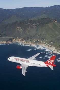 an airplane flying over the ocean with mountains in the background and water below