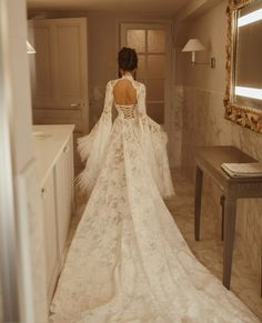 a woman in a white wedding dress is walking into the room with her back to the camera