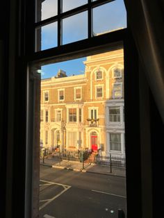 an open window looking out onto a street with buildings on both sides and a red door in the middle