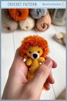 a hand holding a small crocheted lion toy in front of yarn balls and needles