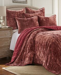 a bed with red comforter and pillows in a room next to a dresser,