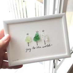 a hand holding up a card with two trees on it and the words joy to the world