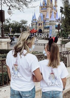 two girls wearing mickey mouse ears standing in front of a castle