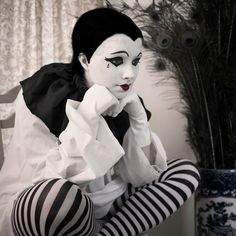 a woman with black and white makeup sitting in front of a vase