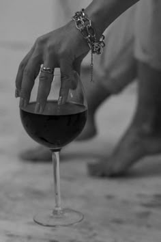 a hand reaching for a wine glass with red wine in it on the floor next to someone's feet