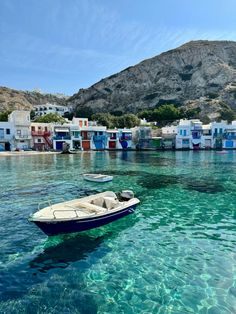 two small boats floating in the clear blue water next to white houses and mountains on either side