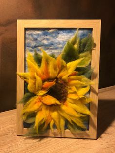 a painting of a yellow sunflower in a wooden frame on a wood table top