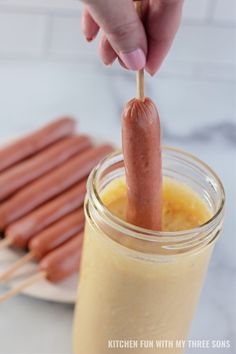 a person holding a hot dog on a stick in a mason jar with other hot dogs behind it