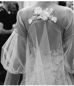 the back of a woman's wedding dress with sheer sleeves and flowers on it