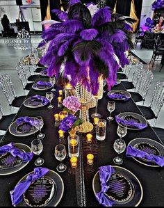 the table is set with purple and gold place settings, silverware, and feathers