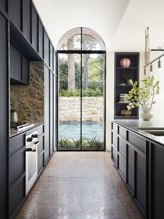 a kitchen with black cabinets and an arched glass door leading to a swimming pool in the background