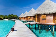 the water is crystal blue and there are many huts on stilts in the water