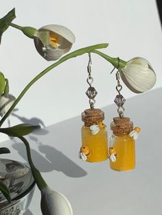 two glass jars with flowers hanging from them on a table next to a potted plant