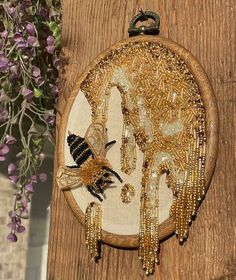 a wooden wall hanging with bead work on it's side and flowers in the background