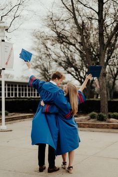 a man and woman in blue graduation gowns holding up their caps while walking down the street