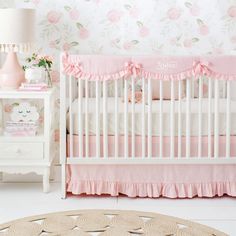 a white crib with pink bedding and flowers on the wall next to it