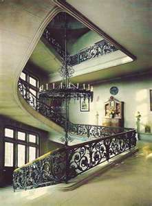 a spiral staircase in an old house with wrought iron railings and chandelier