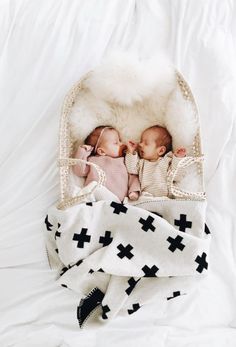 two babies are laying in a basket on top of a white blanket with black crosses