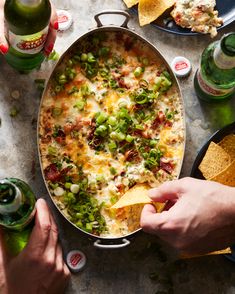 a person is dipping tortilla chips into a large skillet