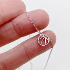 a hand holding a tiny silver necklace with a basketball ball on it's chain