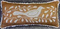 a brown and white embroidered pillow with birds on it's side, sitting on a gray carpet