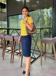 a woman standing in front of a window with her hand on her hip and purse over her shoulder