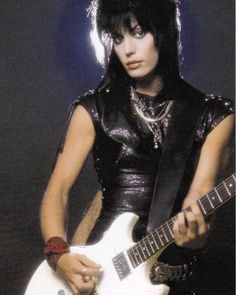 a man with black hair holding a white guitar in his hand and wearing a leather outfit