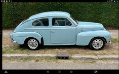 an old blue car parked in front of a hedge