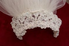 a close up of a white head piece on a red cloth with pearls and tulle