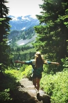 a woman hiking up a trail in the mountains with her arms outstretched and legs spread out