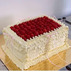 a large cake with white frosting and raspberries on top is sitting on a table