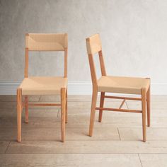 two wooden chairs sitting side by side on a hard wood floor in front of a white wall