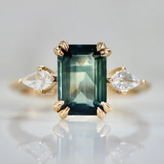 an emerald and diamond ring with three pear shaped diamonds on the side, set in yellow gold